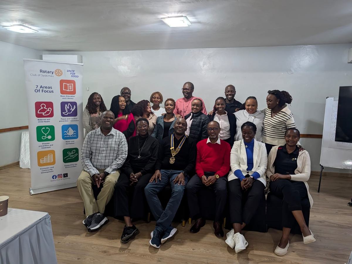 Club members gathered for a group photograph beside the club banner at a Thursday meeting, the president seated at the centre in the club collar.