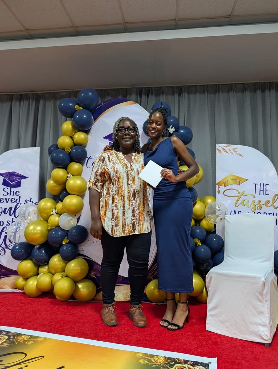 A member standing with a new graduate in front of a navy and gold graduation backdrop.