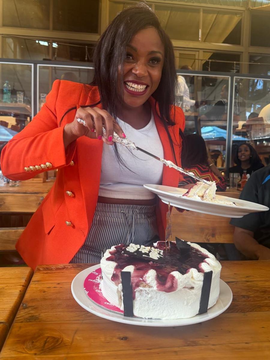 A member in a red blazer lifting the first slice from a birthday cake at a restaurant table.