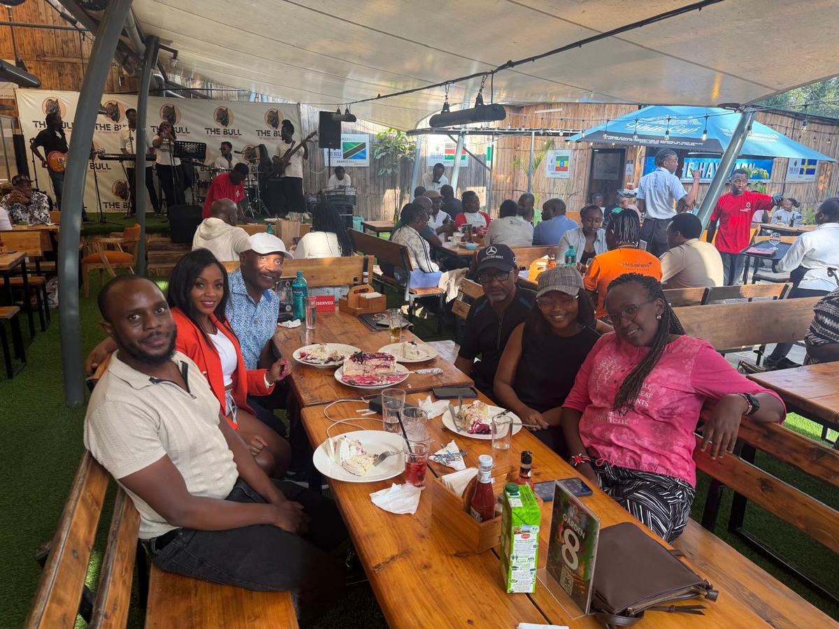 Members along a long wooden table with cake and drinks, a live band playing behind them.