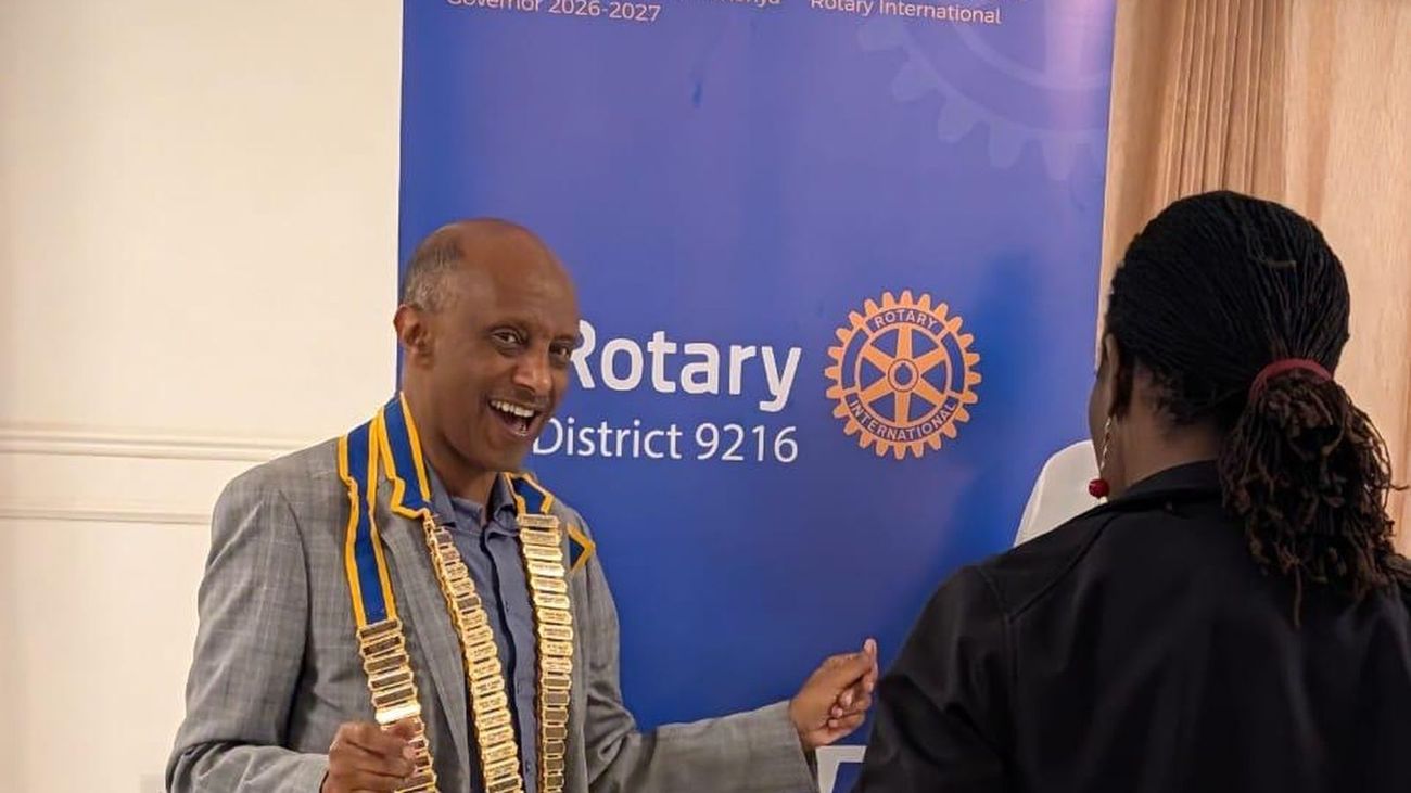 District Governor Esayas Yeyesuswork, wearing the governor’s collar, laughing mid-conversation in front of the District 9216 banner